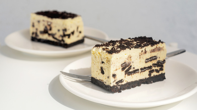 cookies and cream cheesecake bar dessert on white plate with fork with another piece behind it