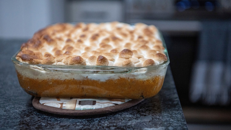 sweet potato casserole topped with marshmallows sitting on a pot holder on a countertop