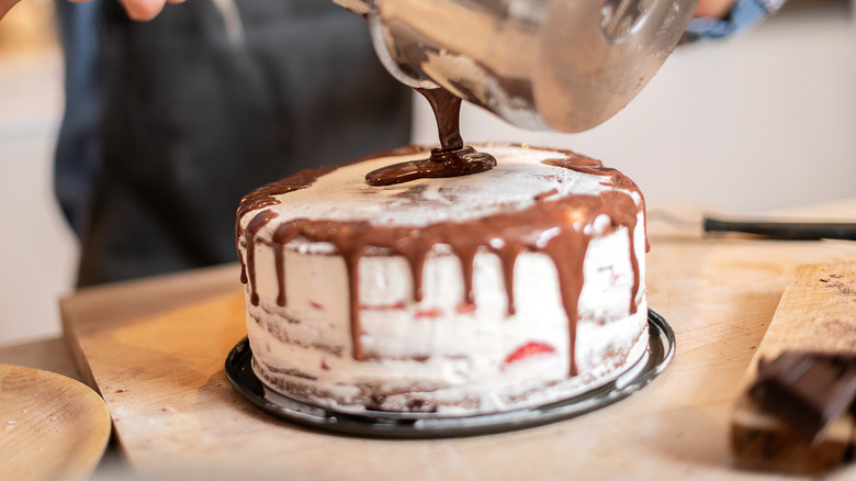 Baker pouring frosting over cake