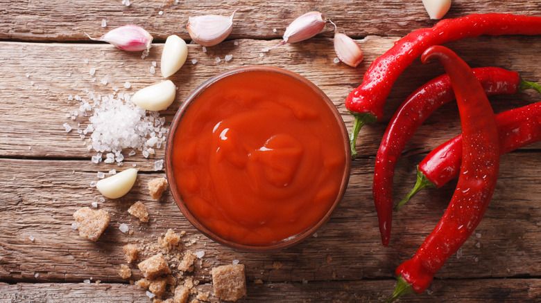 silver bowl filled with red sauce, chili peppers and garlic on wood boards 