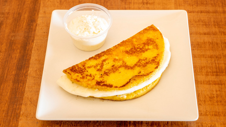 Arepa sandwich with queso fresco and extra cheese on the side on a square white plate