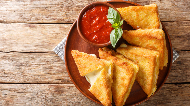 Overhead view of Mozzarella in carrozza sandwiches with a side of marinara on a rustic red plate