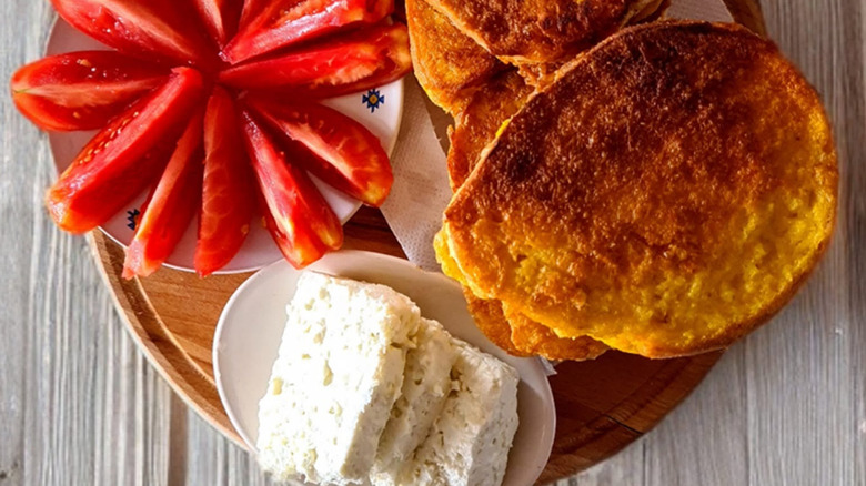 Macedonian Przeni Lepcinja sandwiches with feta cheese and sliced tomatoes on the side on a wooden board