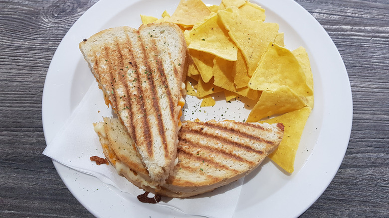 Overhead view of a grilled cheese toastie with a side of tortilla chips on a white plate