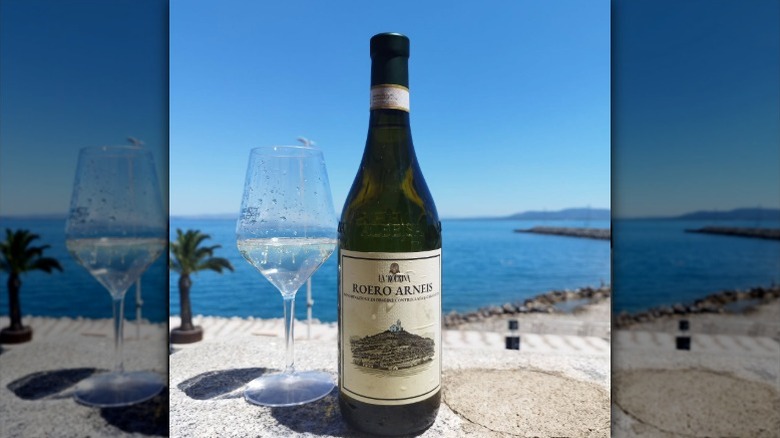 A bottle of arneis wine and a glass sit overlooking a beach