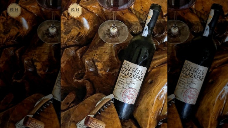 A bottle of okuzgozu wine lies on a polished piece of wood next to a glass and corkscrew