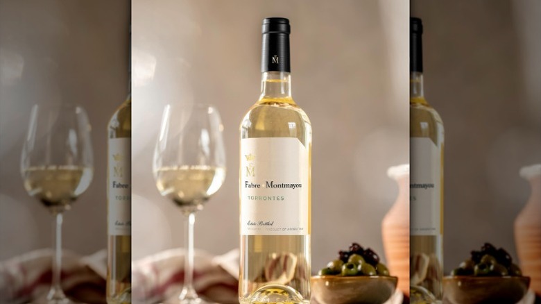 A bottle of torrontes wine sits beside a half-filled glass and a bowl of olives