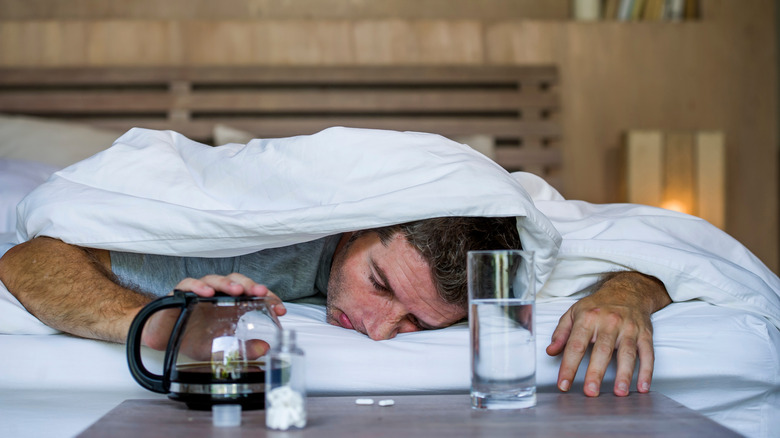 Man in bed with coffee, asprin and water glass