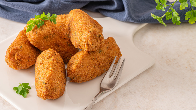 Plate of fried croquettes on white cutting board with fork