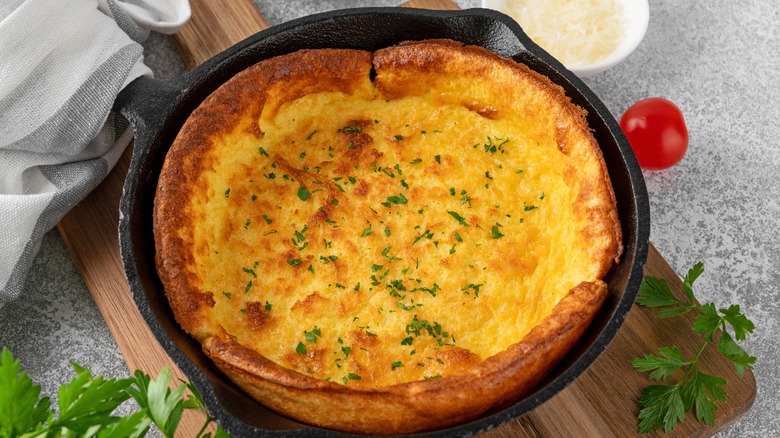 Savory Dutch baby in cast iron skillet on wooden cutting board