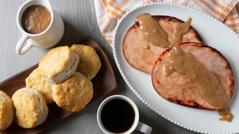 Platter of sliced ham, biscuits, coffee, and gravy on grey table