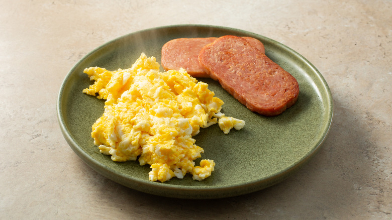 Slices of SPAM next to plate of scrambled eggs