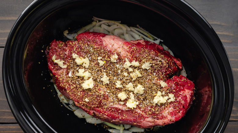 Uncooked beef chuck roast in a black crockpot with onions, garlic, and seasonings