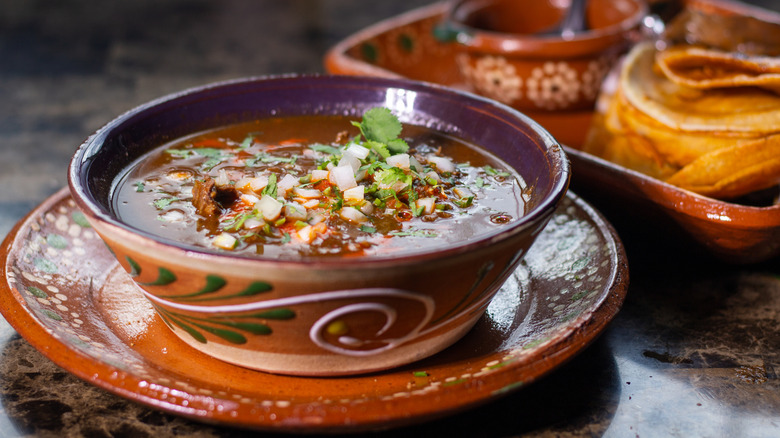 Beef birria with red sauce in a decorative earthenware bowl garnished with pico de gallo