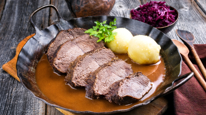 Traditional German Sauerbraten wiht boiled potatoes in a metal pan served with red cabbage