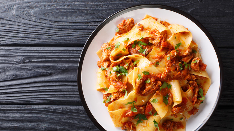 Stracotto over papardelle noodles on a white plate with a black rim
