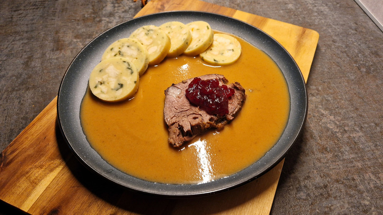 Svíčková na smetaně with bread dumplings on a black plate perched on a wooden cutting board