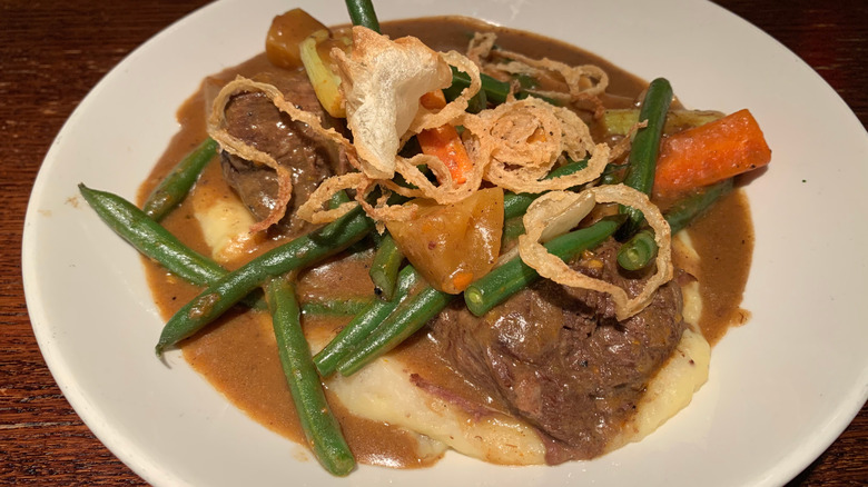 Yankee pot roast served over mashed potatoes on a white plate with green beans and carrot chunks