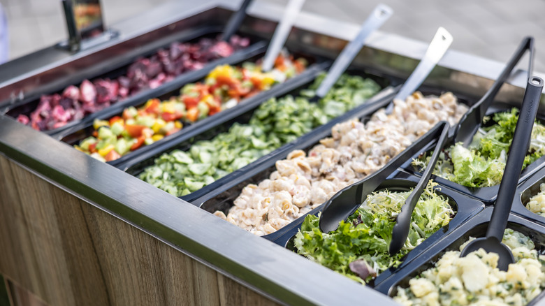A salad bar with a long serving spoon in each dish
