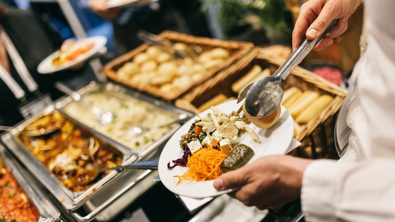 A hand putting food on a plate from a buffet
