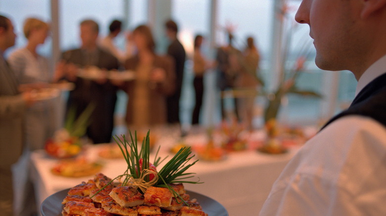 A server at a buffet holding a plate of food with people in the background