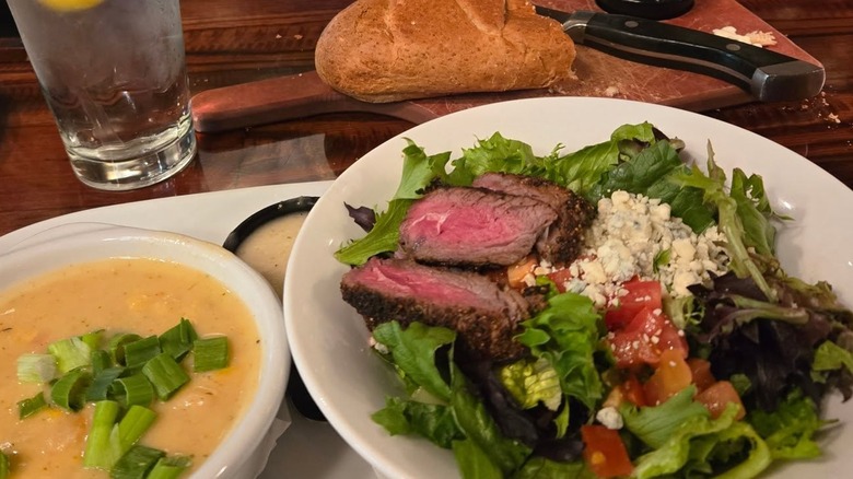 Steak salad on a plate next to a soup and bread