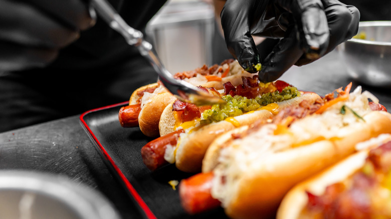 Person adding various toppings to hot dogs
