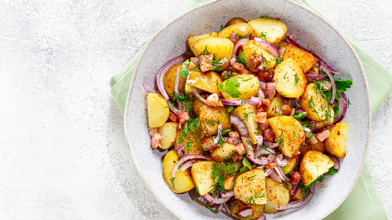 Potato salad in bowl with red onion, corn and herbs