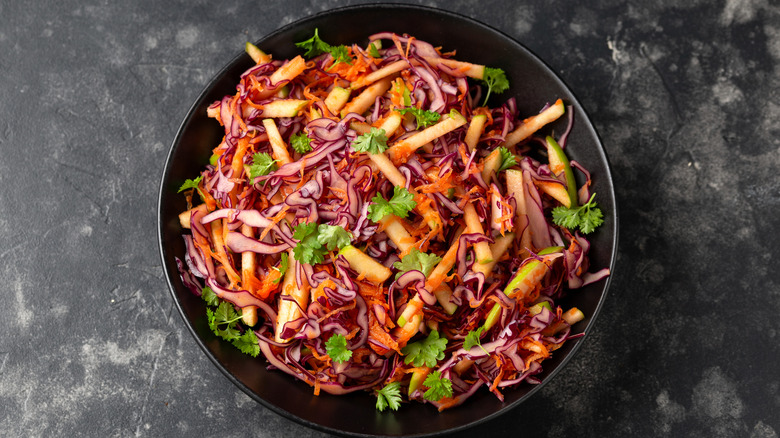 Red cabbage with apples and carrots in black bowl on slate counter