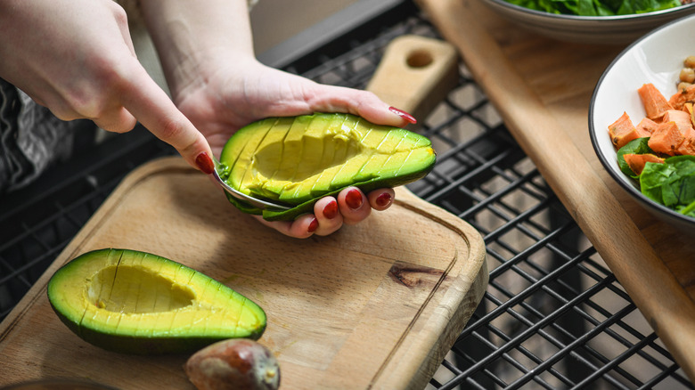Someone slicing and scooping avocados out of their rinds.