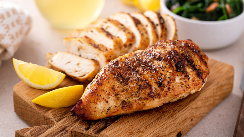 Grilled chicken on a wooden board with lemon wedges.