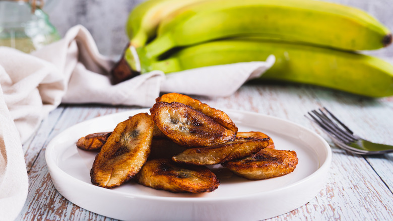 Fried plantains in front of a ripe bunch of plantains.