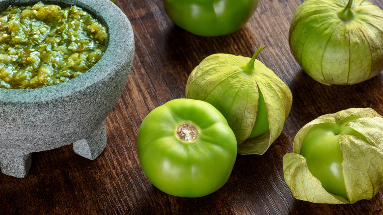 Tomatillos next to a stone bowl of green salsa.