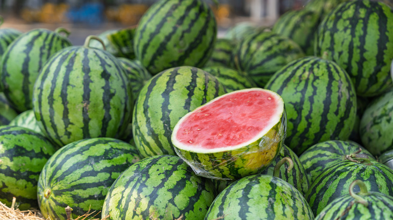 A sliced watermelon sits on top of other watermelons.