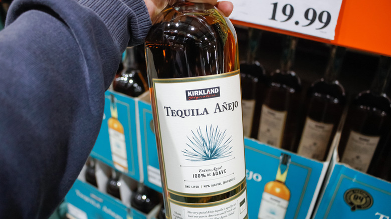 A hand holds a bottle of Kirkland Signature Tequila Anejo