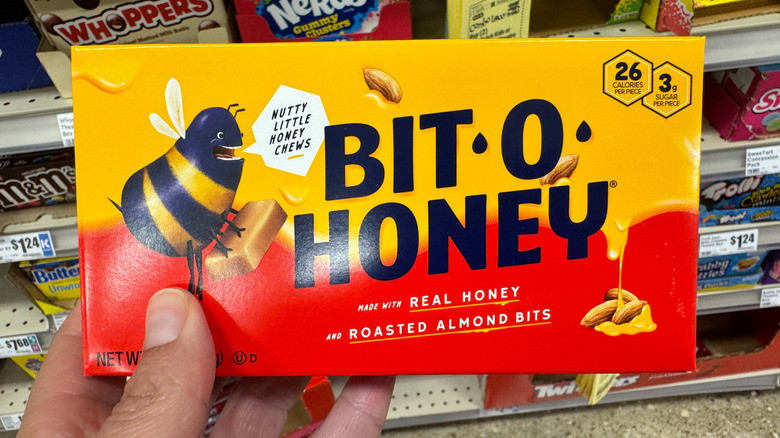 A person holds a box of Bit-o-Honey candy in a candy aisle