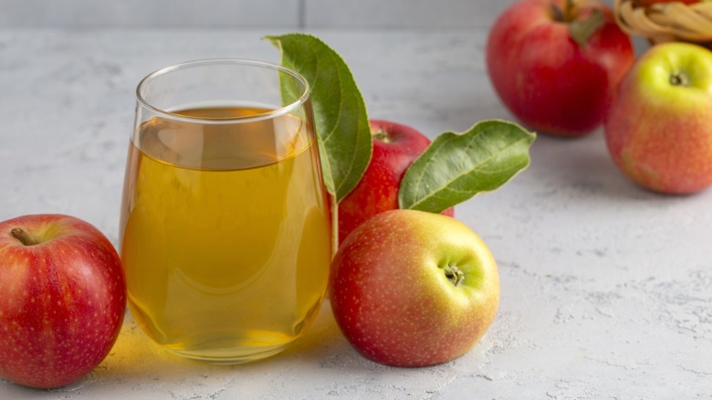 A glass of apple juice surrounded by fresh apples