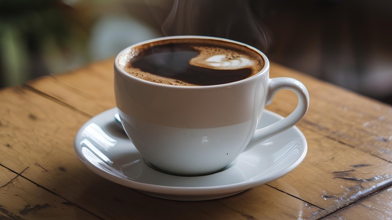 a clear glass cup of black coffee with whole beans scattered around it