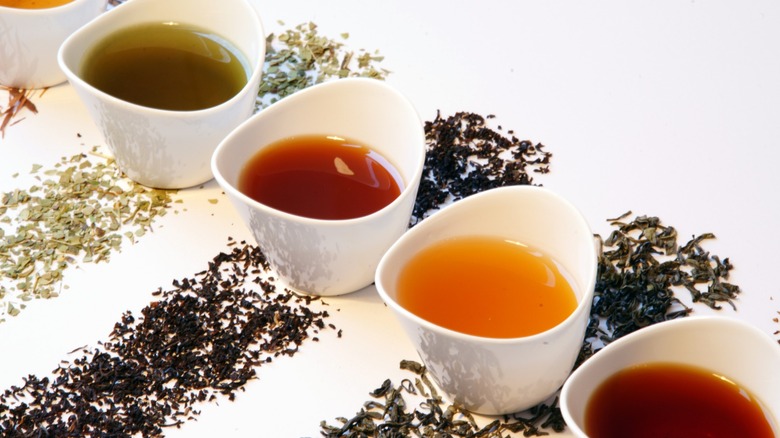 white modern tea cups with different color teas brewed and different tea leaves beside each to signify the brew