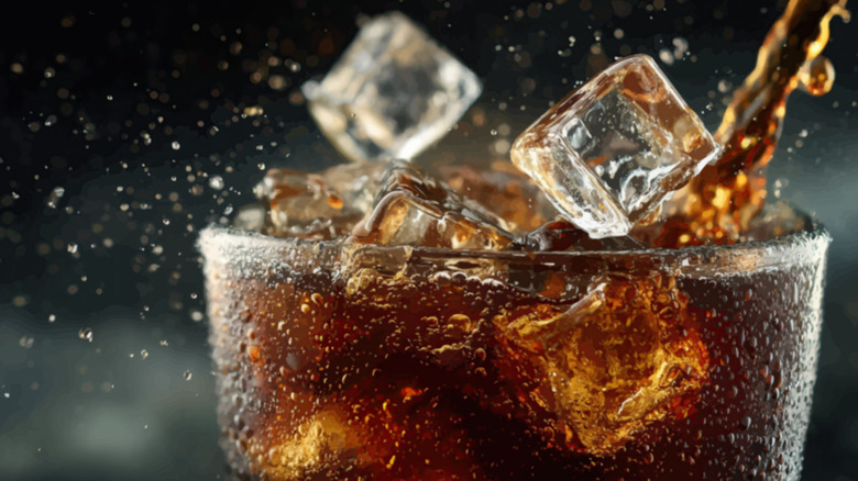 a glass with cold dark cola and ice cubes splashing in