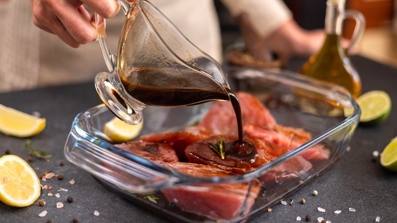 a dark marinade being poured over steaks in a glass baking sheet