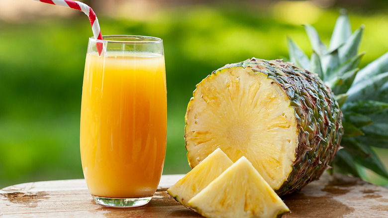 a glass of pineapple juice beside a fresh pineapple cut in half with two wedges