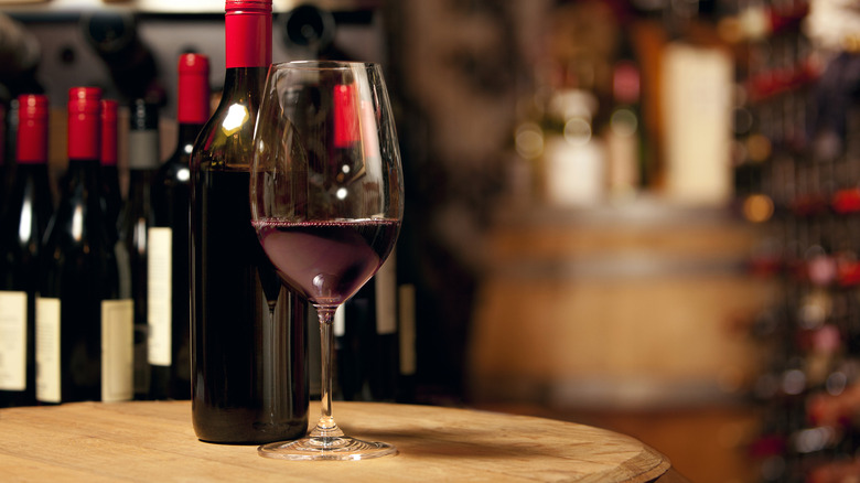 a glass of red wine in front of many bottles of red wine