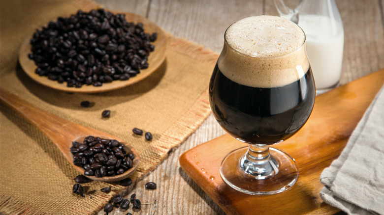 a glass of foamy dark beer on a wooden cutting board