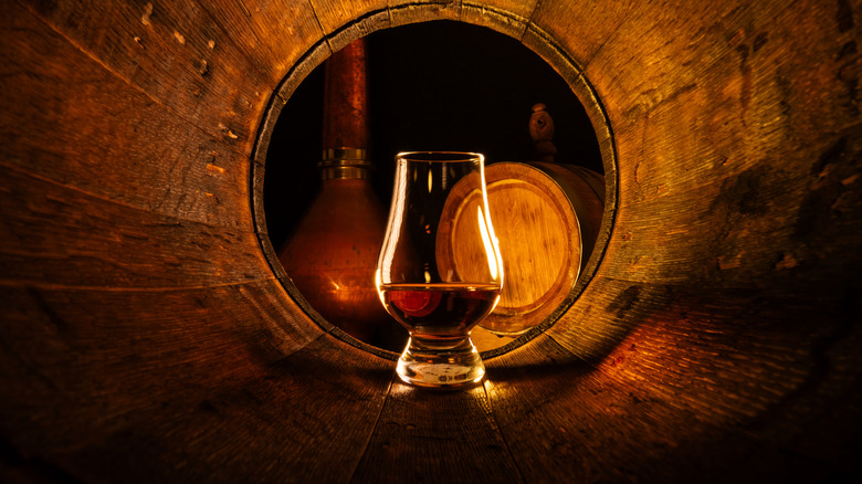 a glass of scotch whiskey in an oak barrel