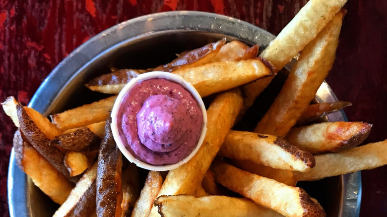 A cup of blueberry ketchup next to a plate of fries