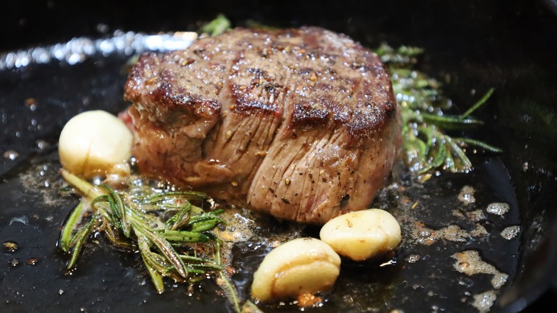 Seared filet mignon in cast iron pan with butter and seasoning