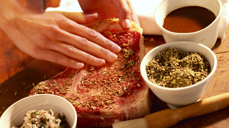 Hands rubbing seasonings into raw steak
