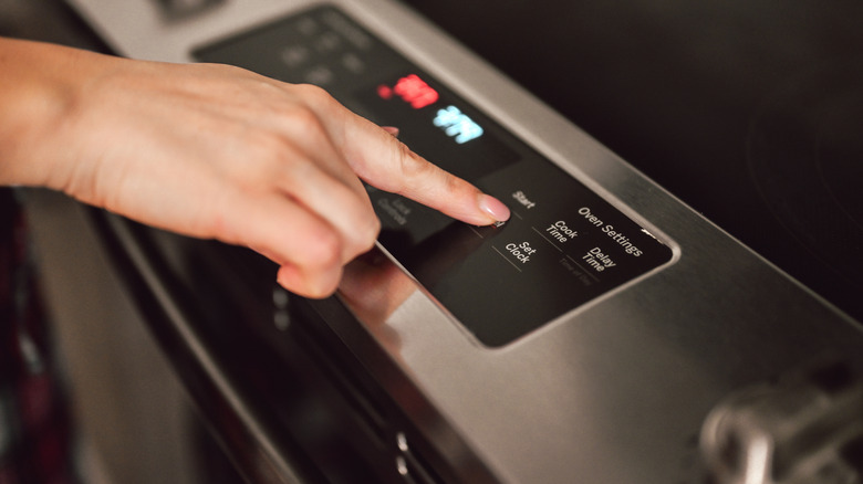 Person's hand pressing start button on an oven