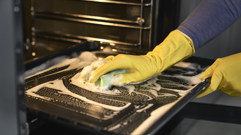 Person wearing plastic gloves cleaning an oven with a soapy sponge
